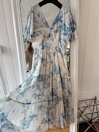 A blue and white floral dress displayed on a mannequin against a white wooden background.