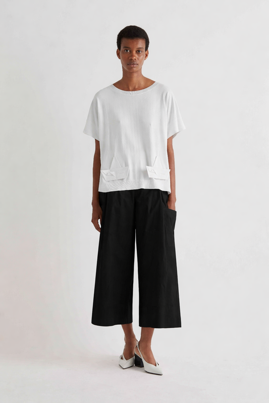 Person wearing a white oversized t-shirt and black wide-leg pants on a white background